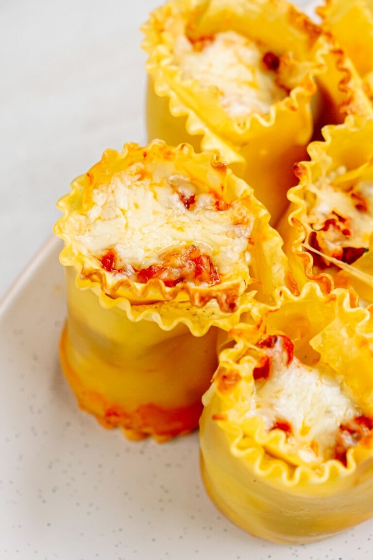 Close-up of five lasagna roll-ups filled with cheese and tomato sauce, served on a white plate. These delightful lasagna roll-ups resemble tasty lasagna cups, perfect for individual servings.
