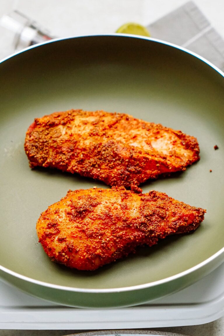 Two seasoned chicken breasts are cooking in a non-stick frying pan.