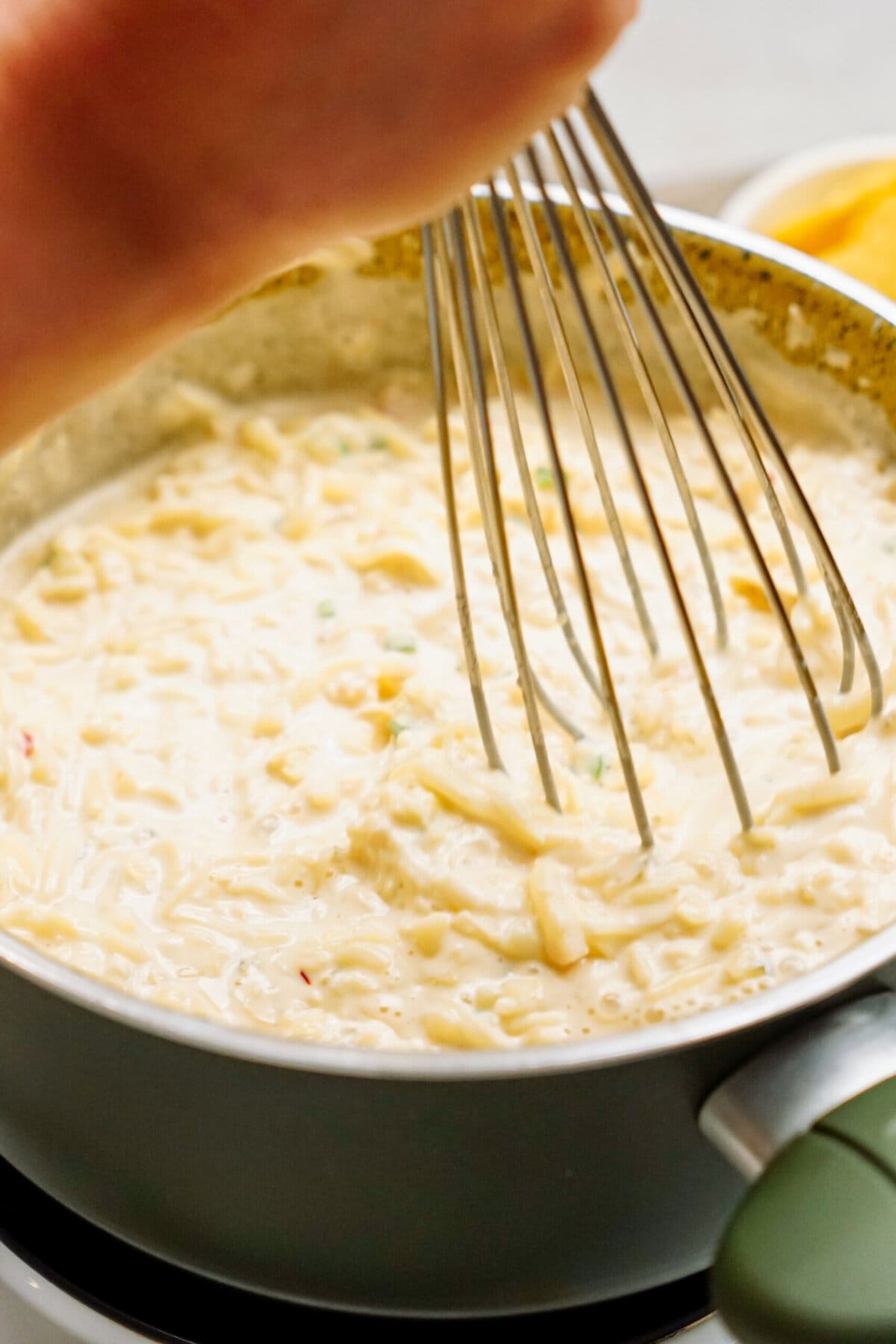 A hand is using a whisk to stir creamy queso in a saucepan on a stovetop.