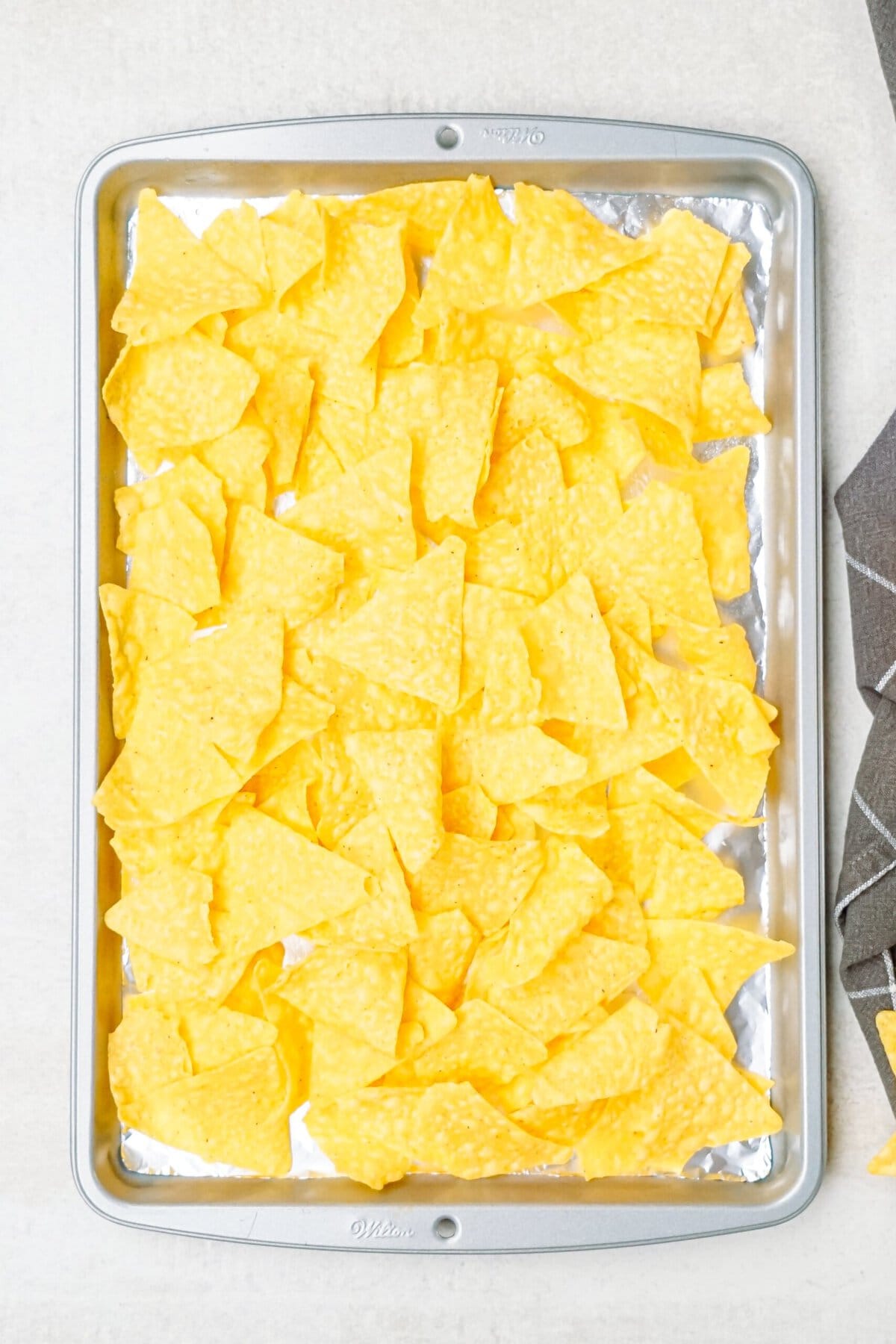 A baking sheet filled with a single layer of uncooked yellow tortilla chips.