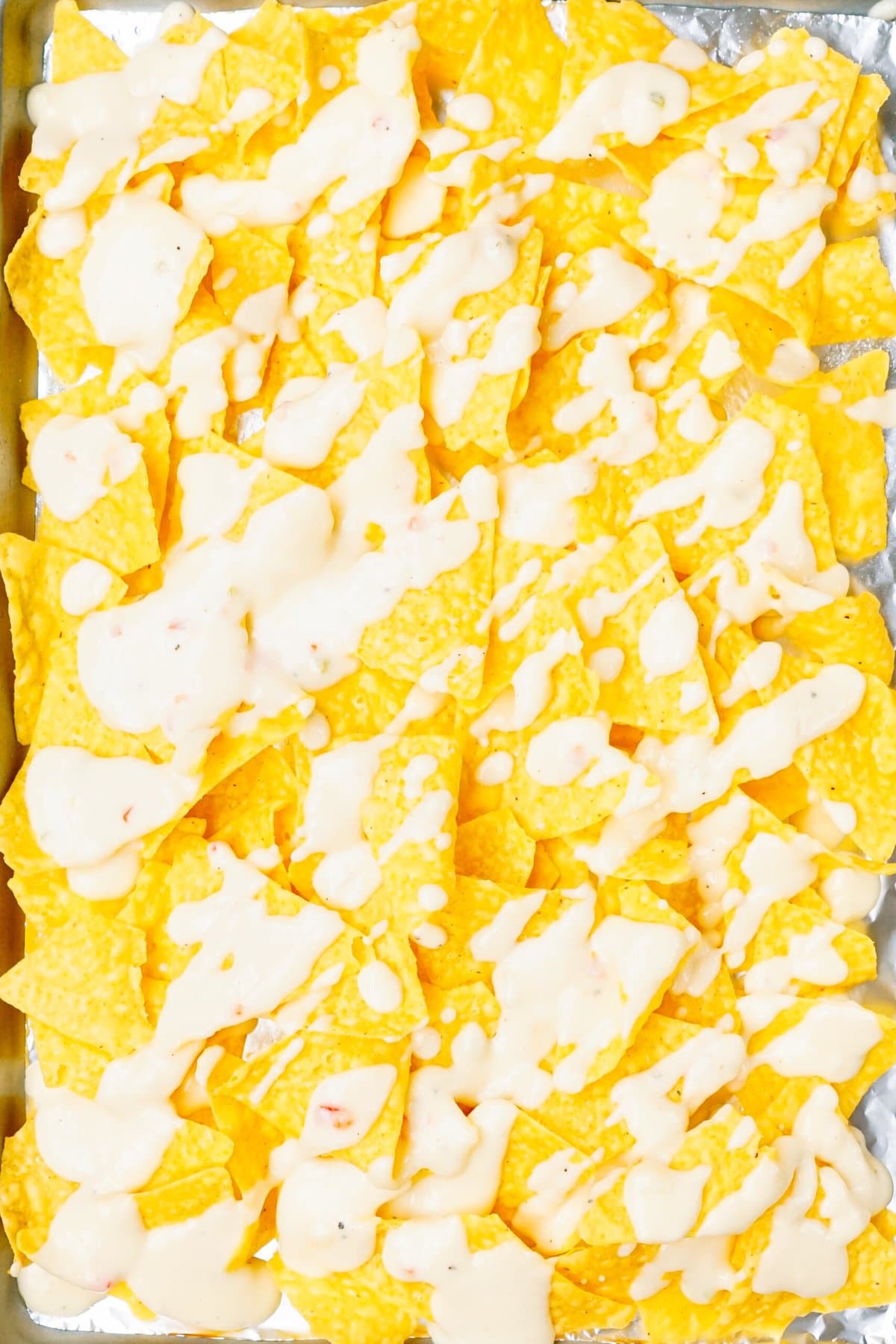 A tray of yellow tortilla chips covered in melted white cheese.