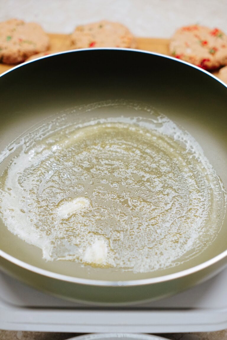 A frying pan with melted butter preparing for cooking. In the background, while nearby tuna patties wait to be crafted into a delicious meal.