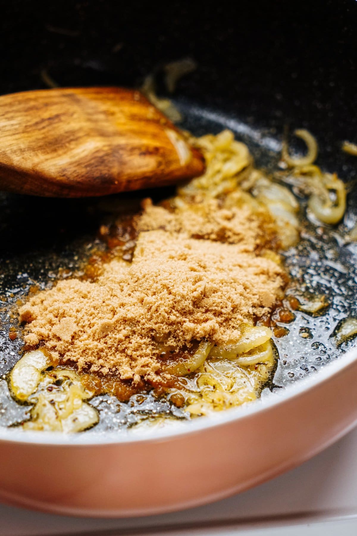 A wooden spatula in a frying pan with partially caramelized onions, a mound of brown sugar, and the promise of creamy goat cheese truffles.