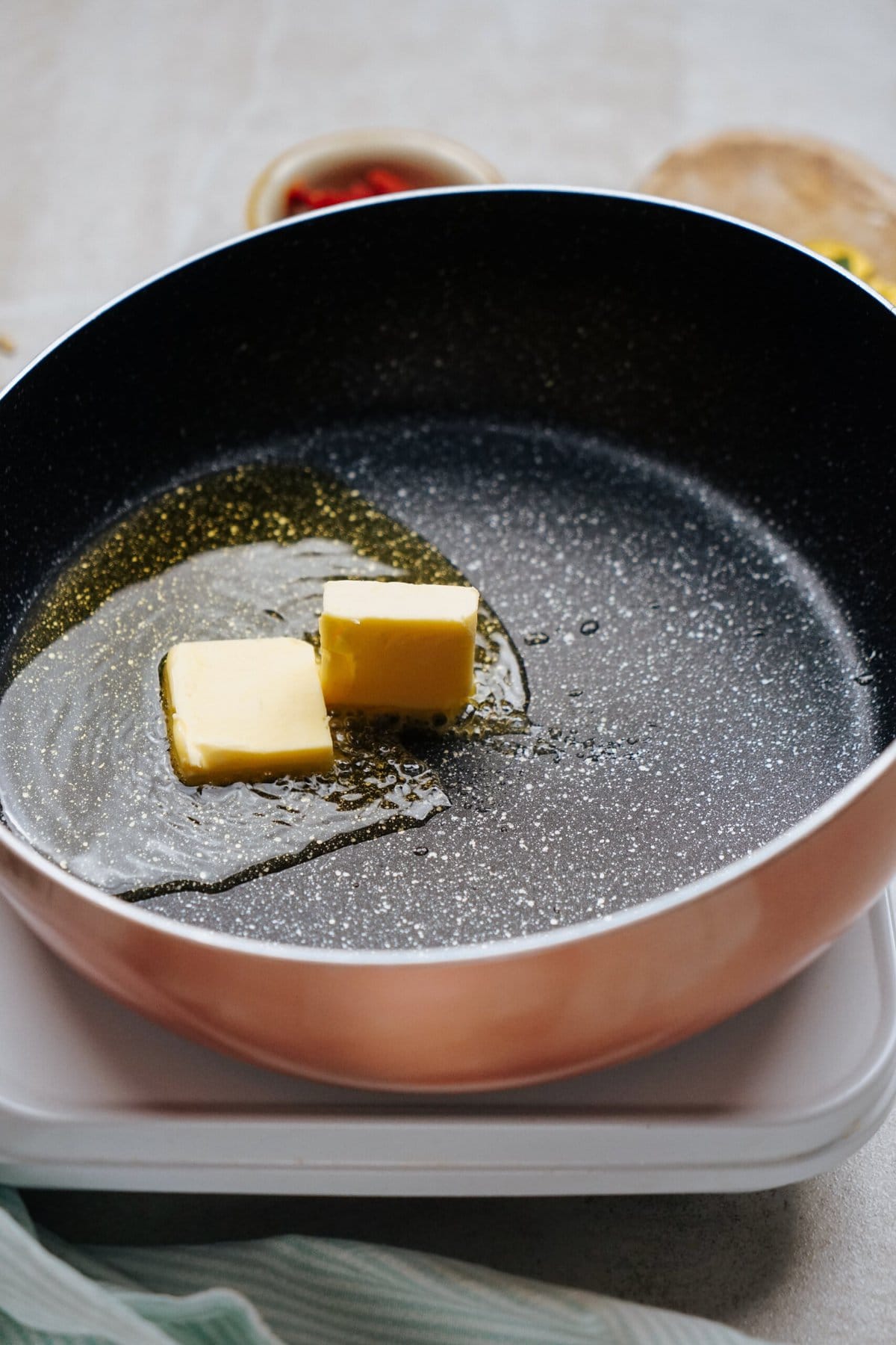 Two cubes of butter melting in a black non-stick frying pan.