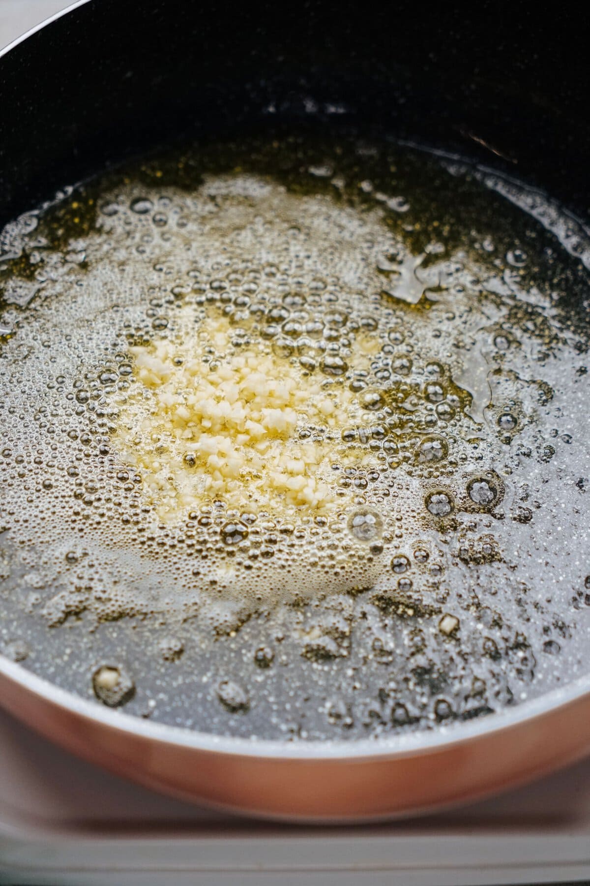 A frying pan with chopped garlic sizzling in melted butter.