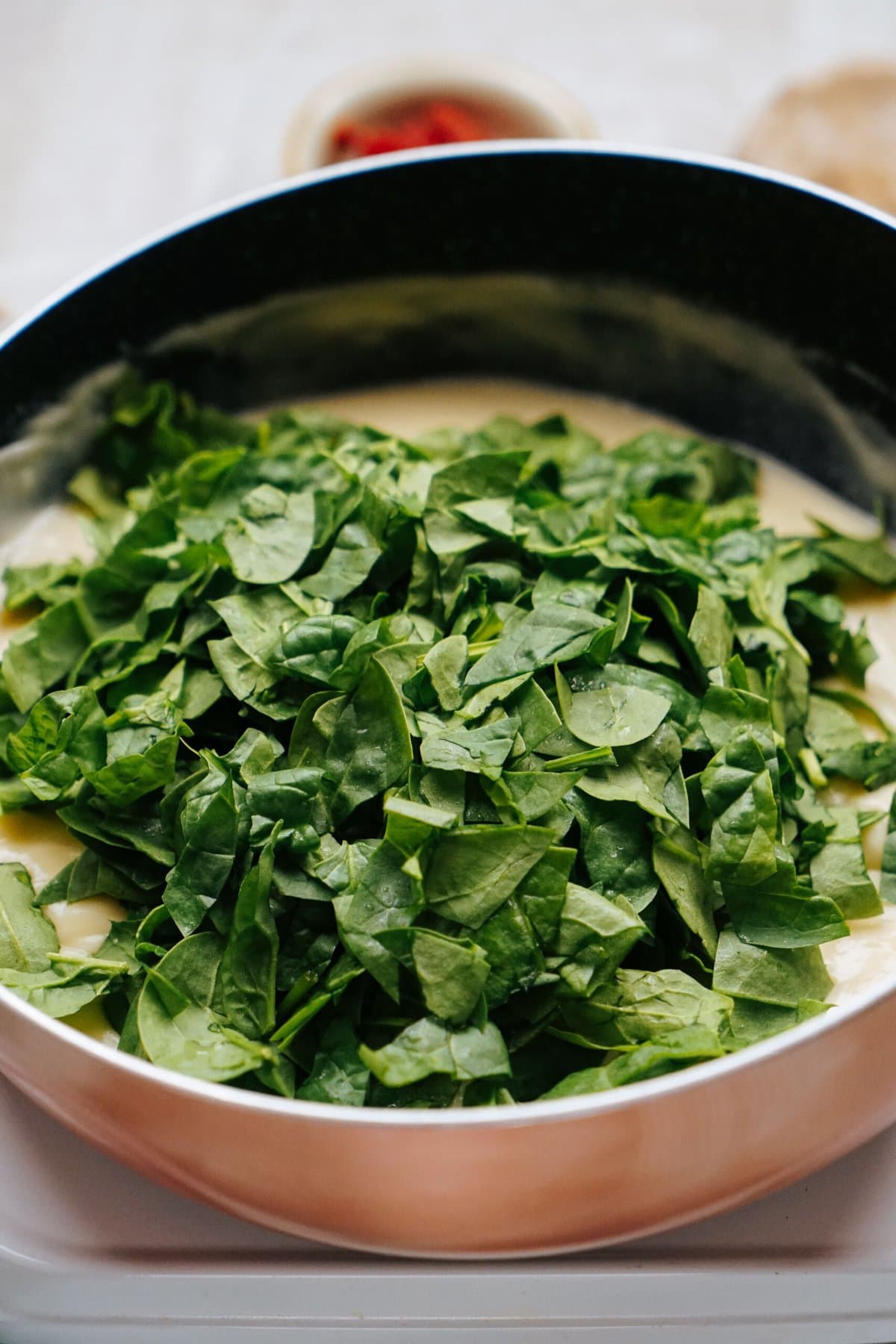 A pan filled with creamy mixture topped with a generous amount of chopped fresh spinach leaves.