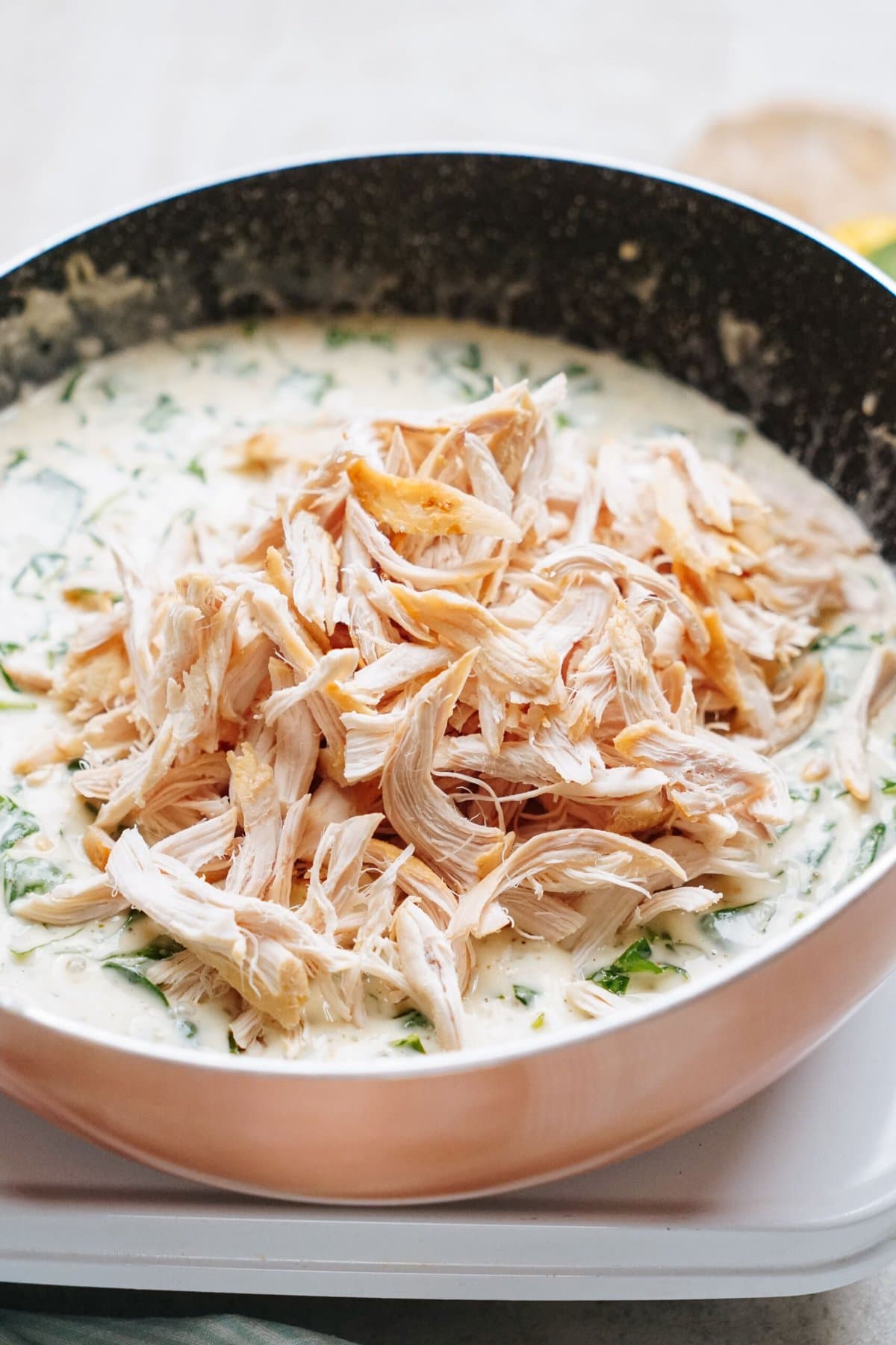 A pan filled with a creamy sauce containing chopped spinach is topped with shredded cooked chicken.