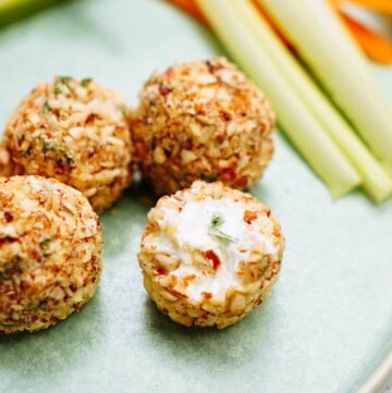 Four nut-coated goat cheese truffles on a plate with sliced vegetables in the background.