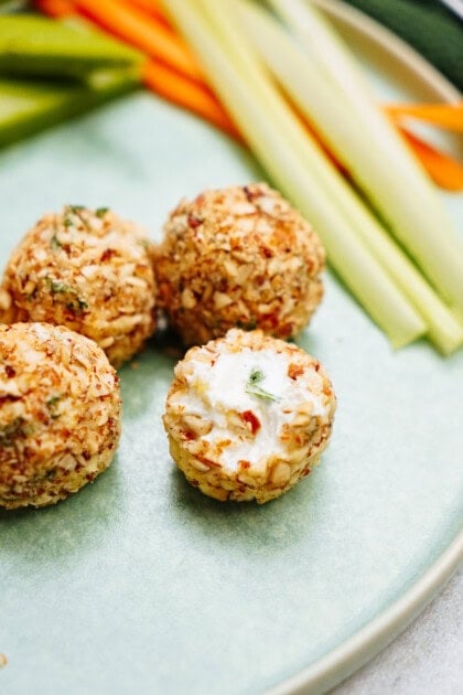 Four nut-coated goat cheese truffles on a plate with sliced vegetables in the background.