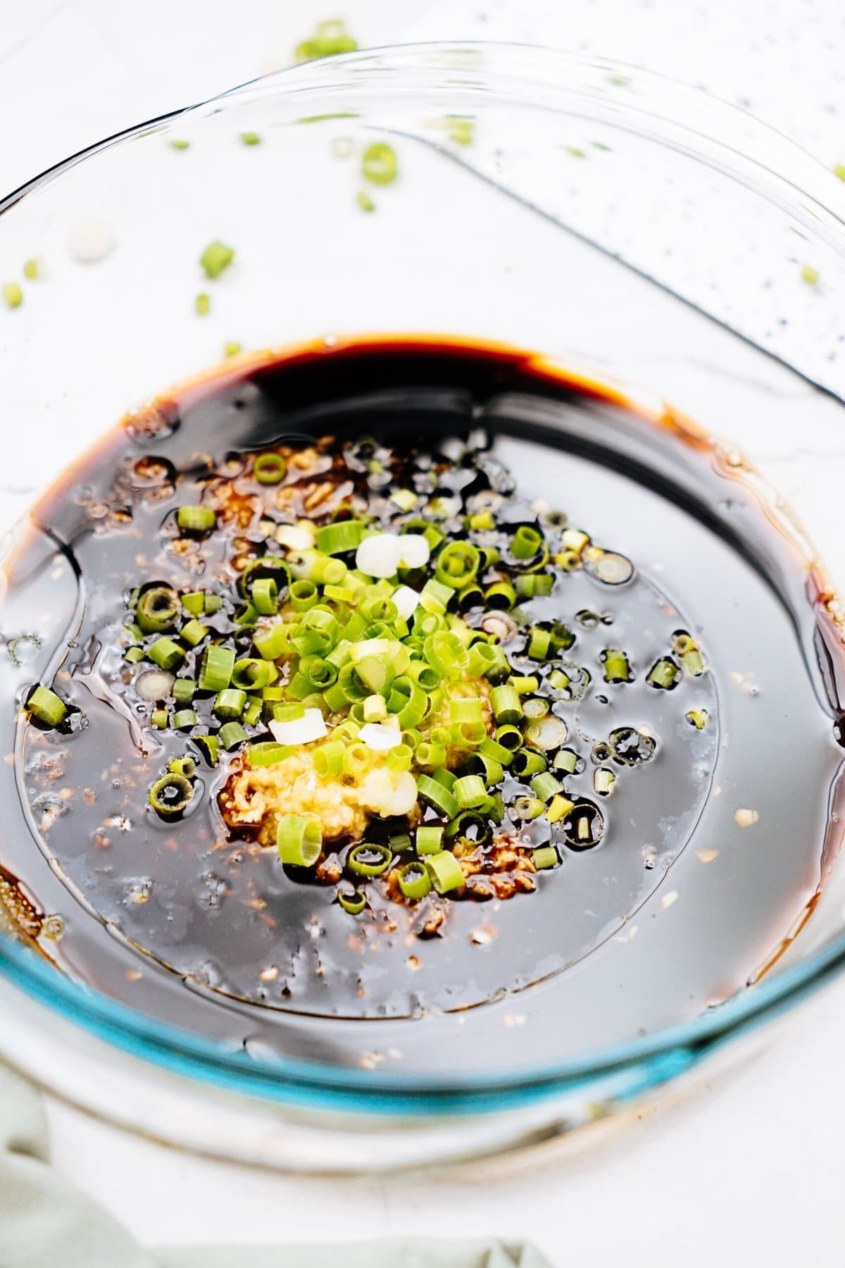 A glass bowl filled with dark soy sauce mixed with chopped green onions and minced garlic, perfect for drizzling over Korean chicken.