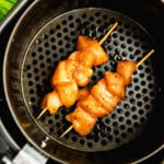 Two raw, seasoned chicken skewers placed in an air fryer basket ready for cooking.