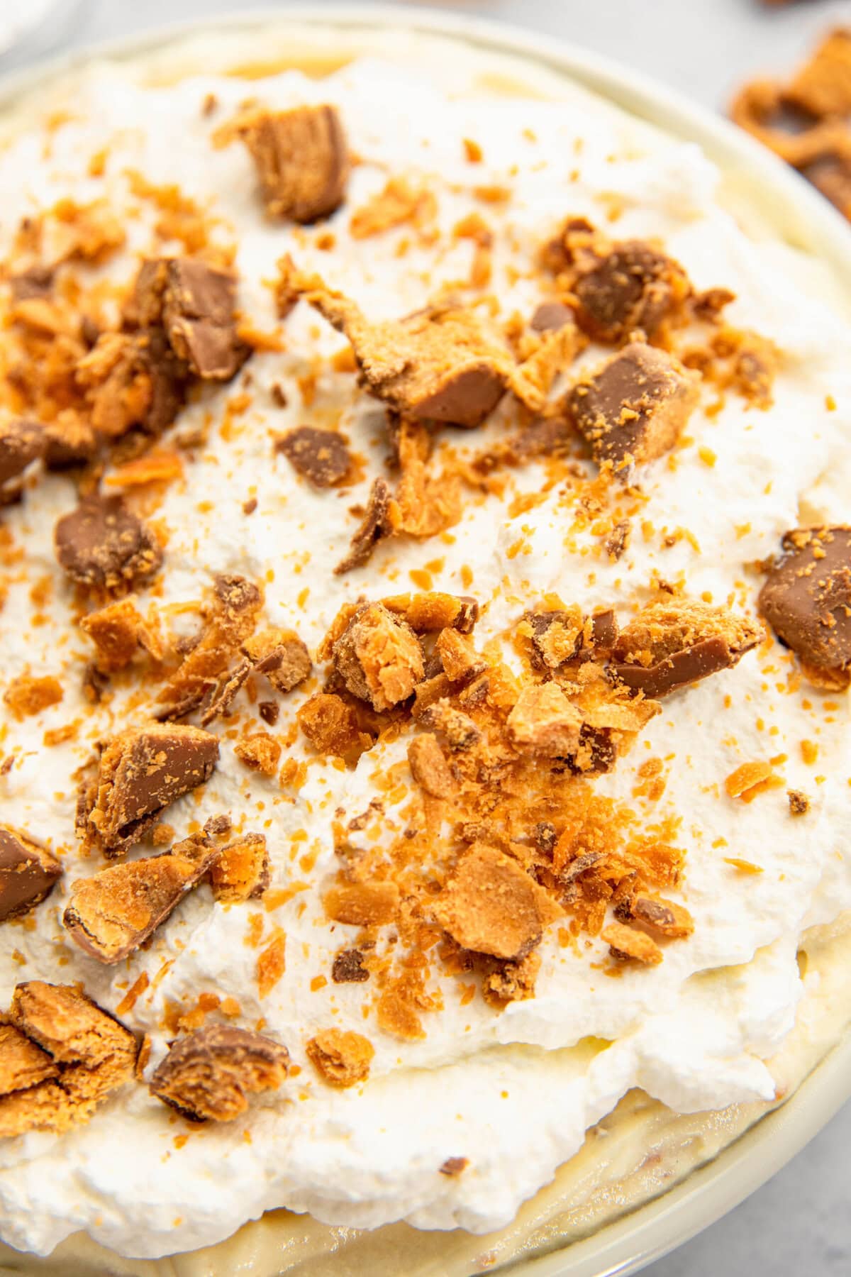 Close-up of a dessert topped with whipped cream and garnished with crumbled pieces of chocolate and caramel.