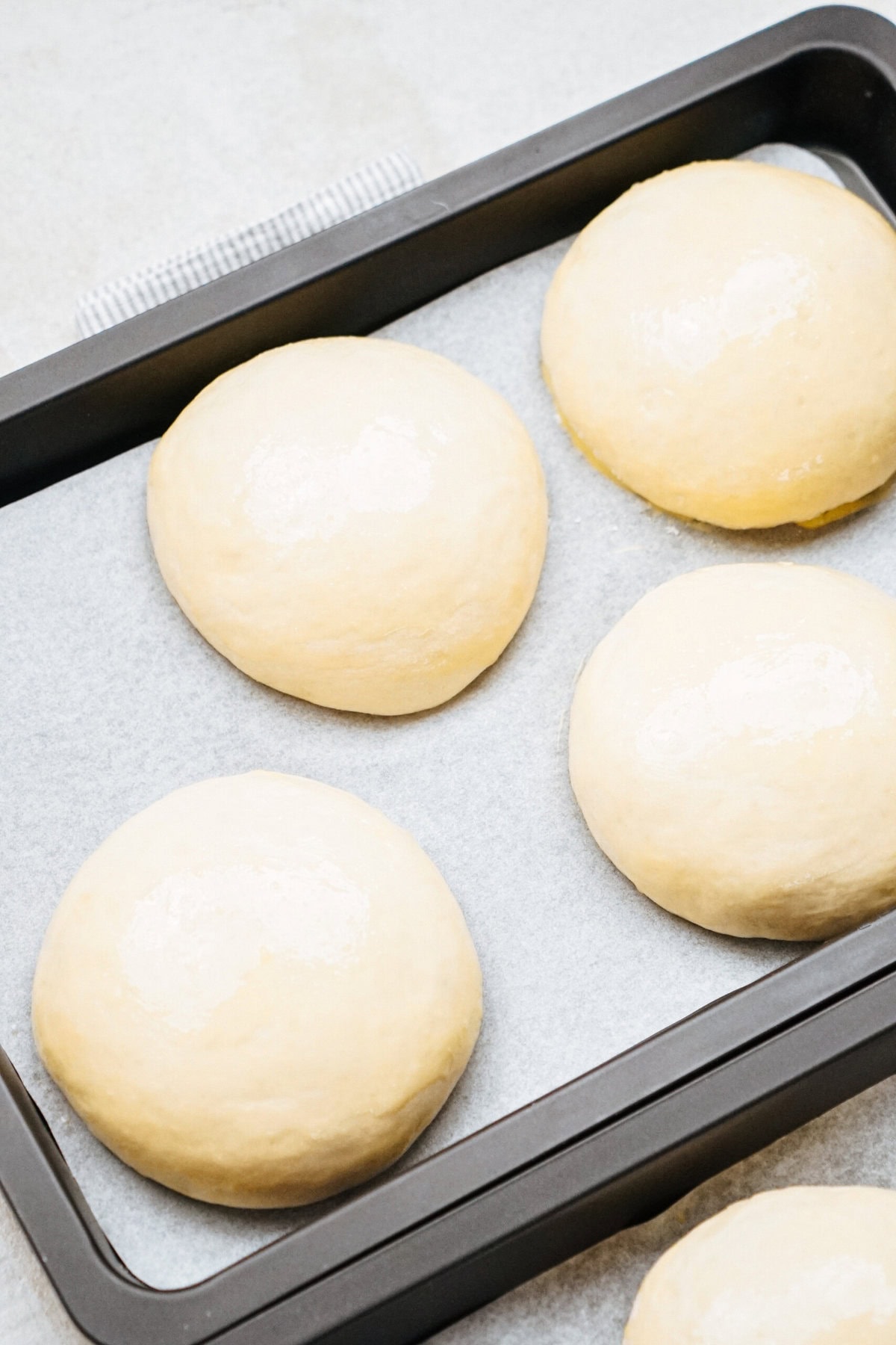 Four unbaked dough balls on a parchment-lined baking sheet, ready to be baked.