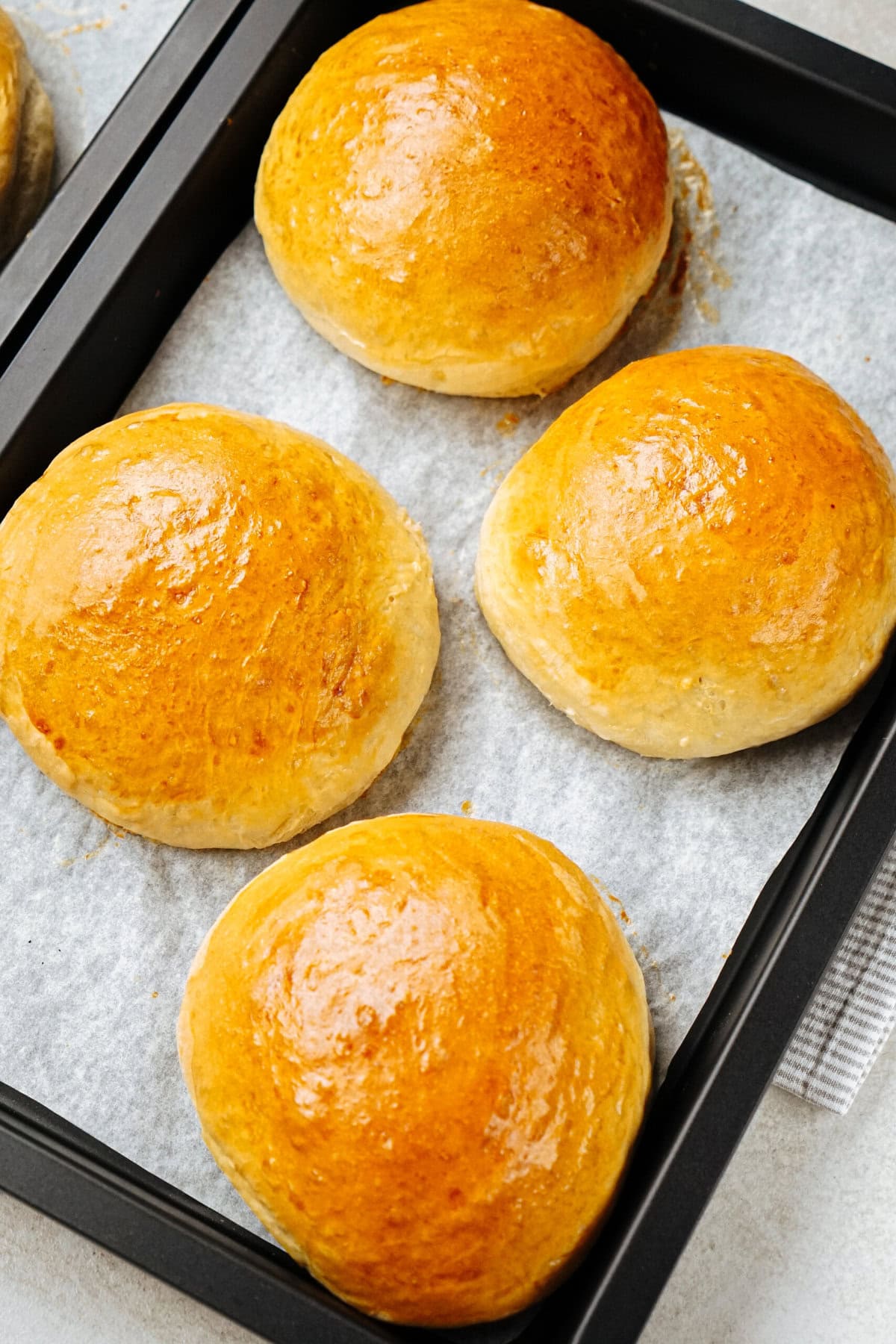 Four golden brown buns on a parchment-lined baking tray.