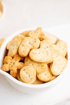 A white bowl filled with various shaped crackers, including hearts and flowers, on a light background.