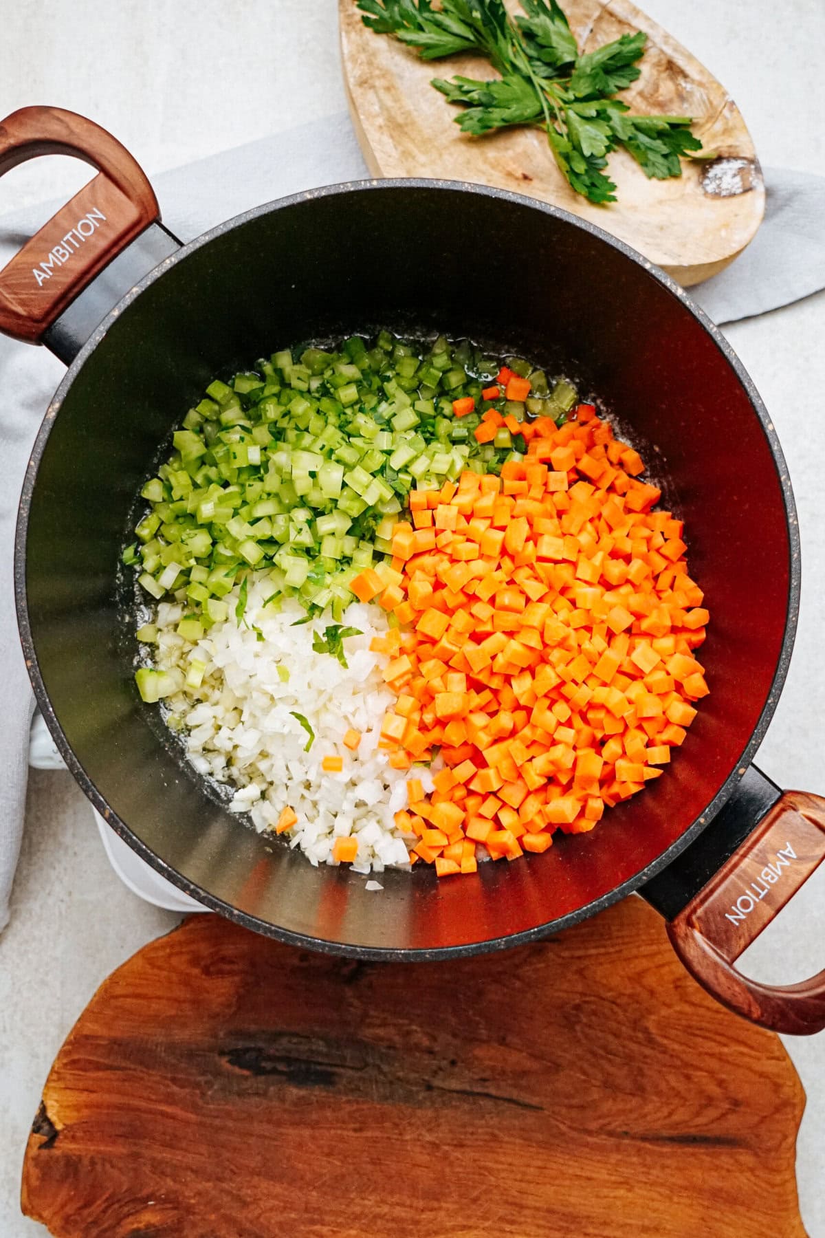 A pot contains diced celery, carrots, and onions arranged separately, ready for a hearty chicken corn chowder. Fresh parsley lies on a cutting board nearby.