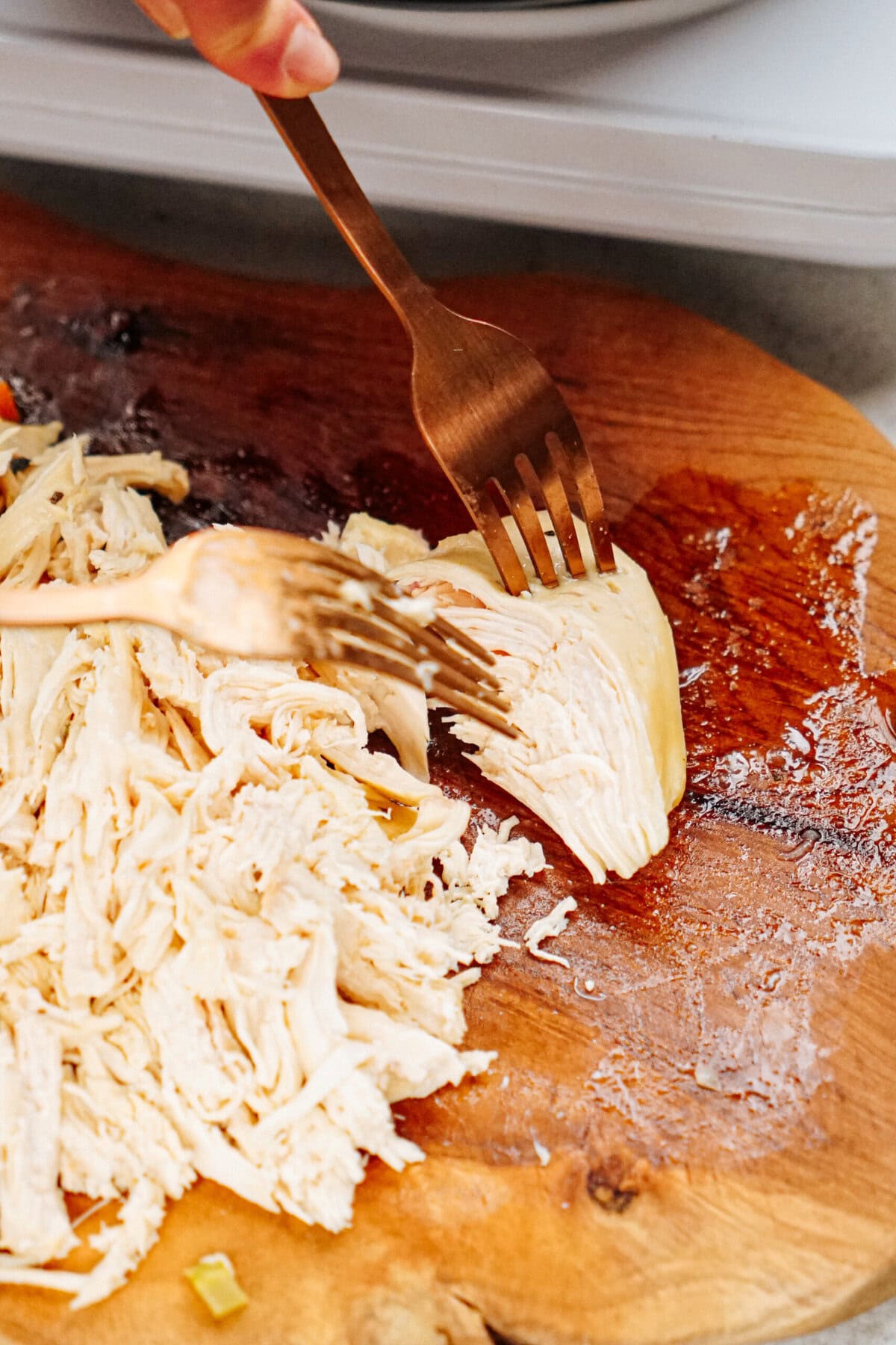 Two forks are shredding cooked chicken on a wooden cutting board, ready to be added to a comforting chicken corn chowder.