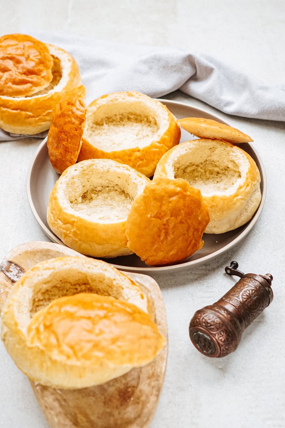 Several hollowed-out bread bowls with golden crusts are arranged on a plate next to a pepper mill on a light surface.
