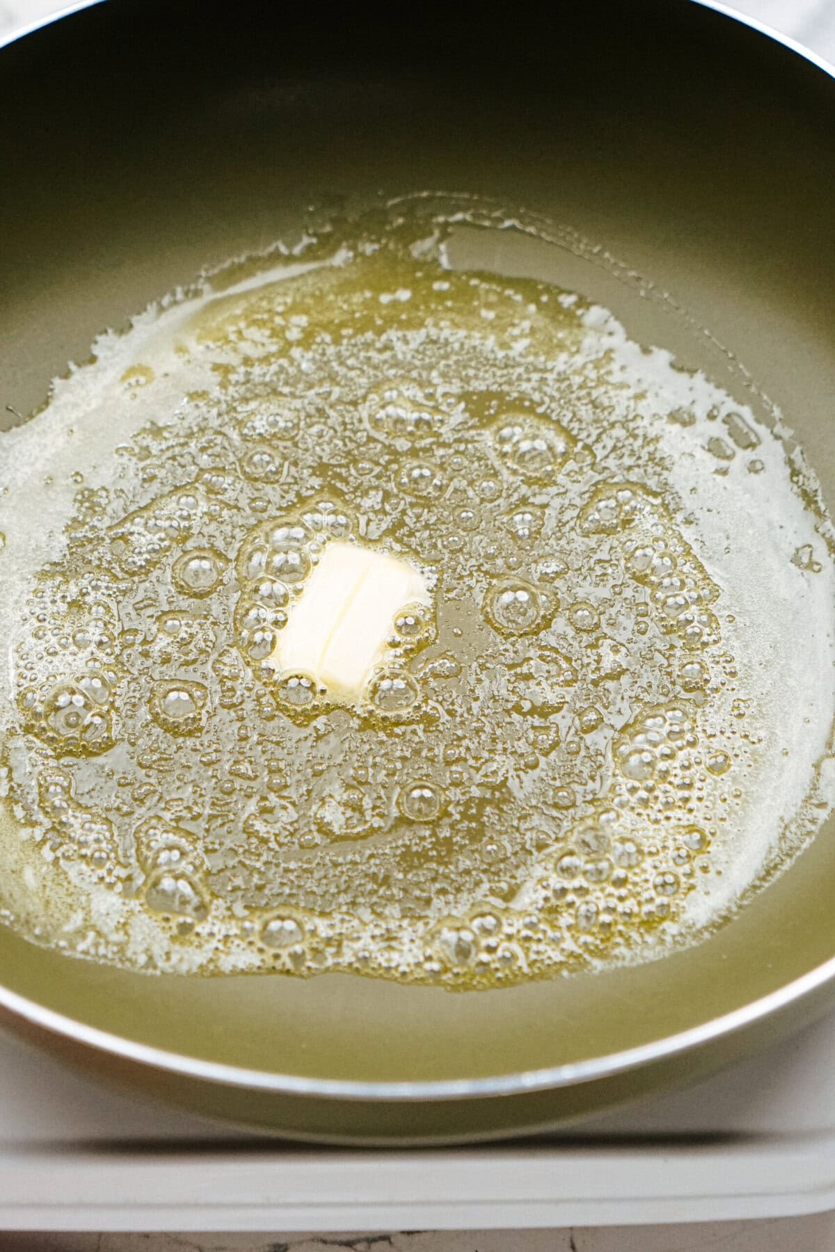 A piece of butter melting and bubbling in a hot frying pan.