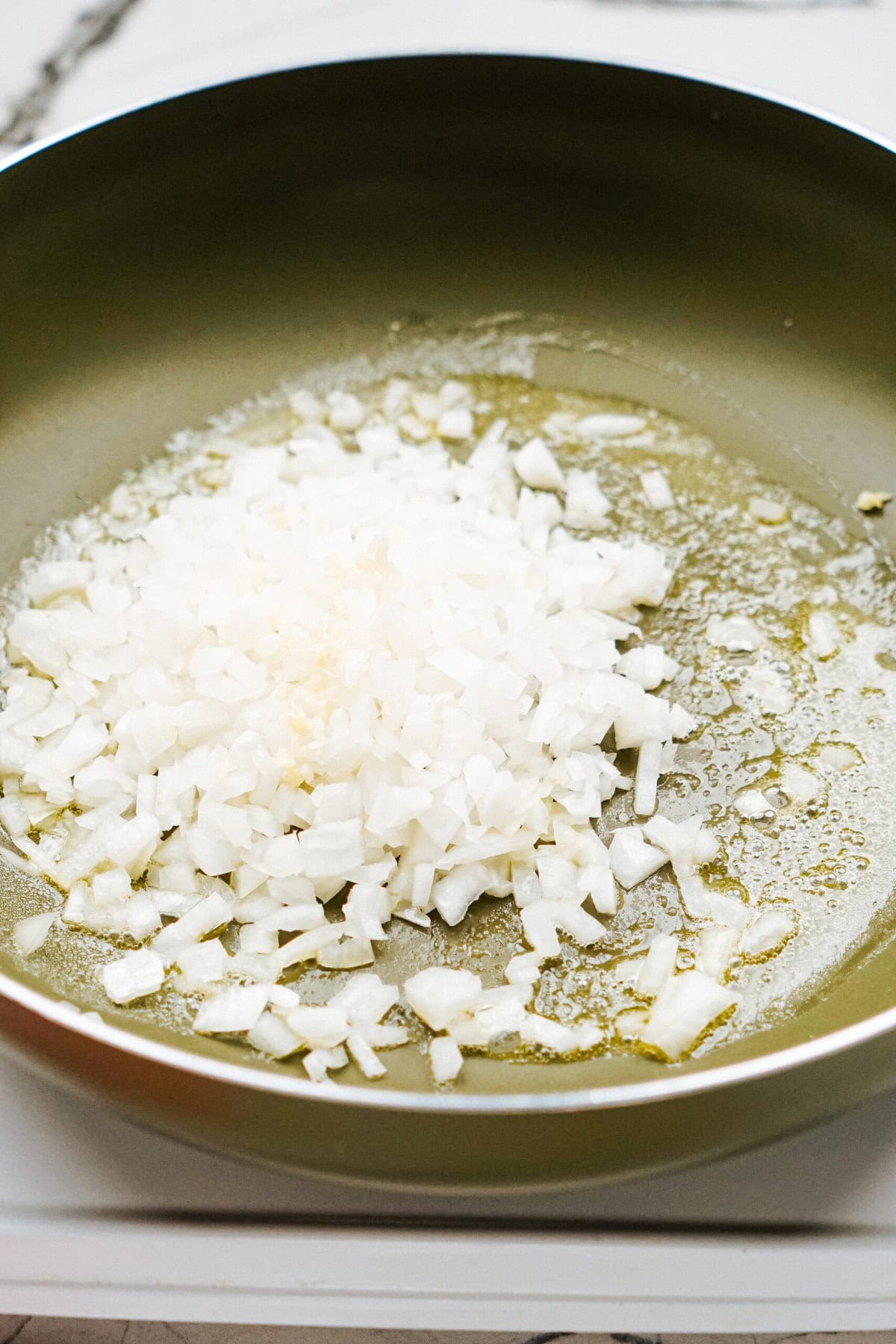 Chopped onions being sautéed in a green frying pan with oil.