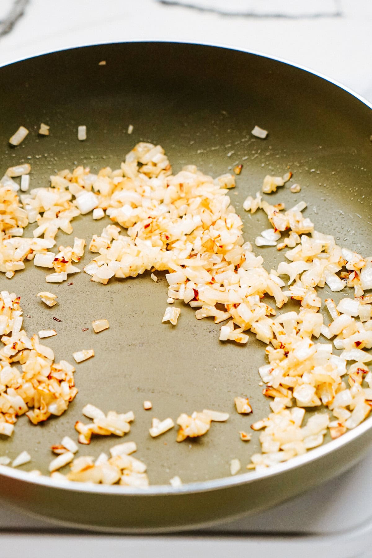 Chopped onions being sautéed in a frying pan.