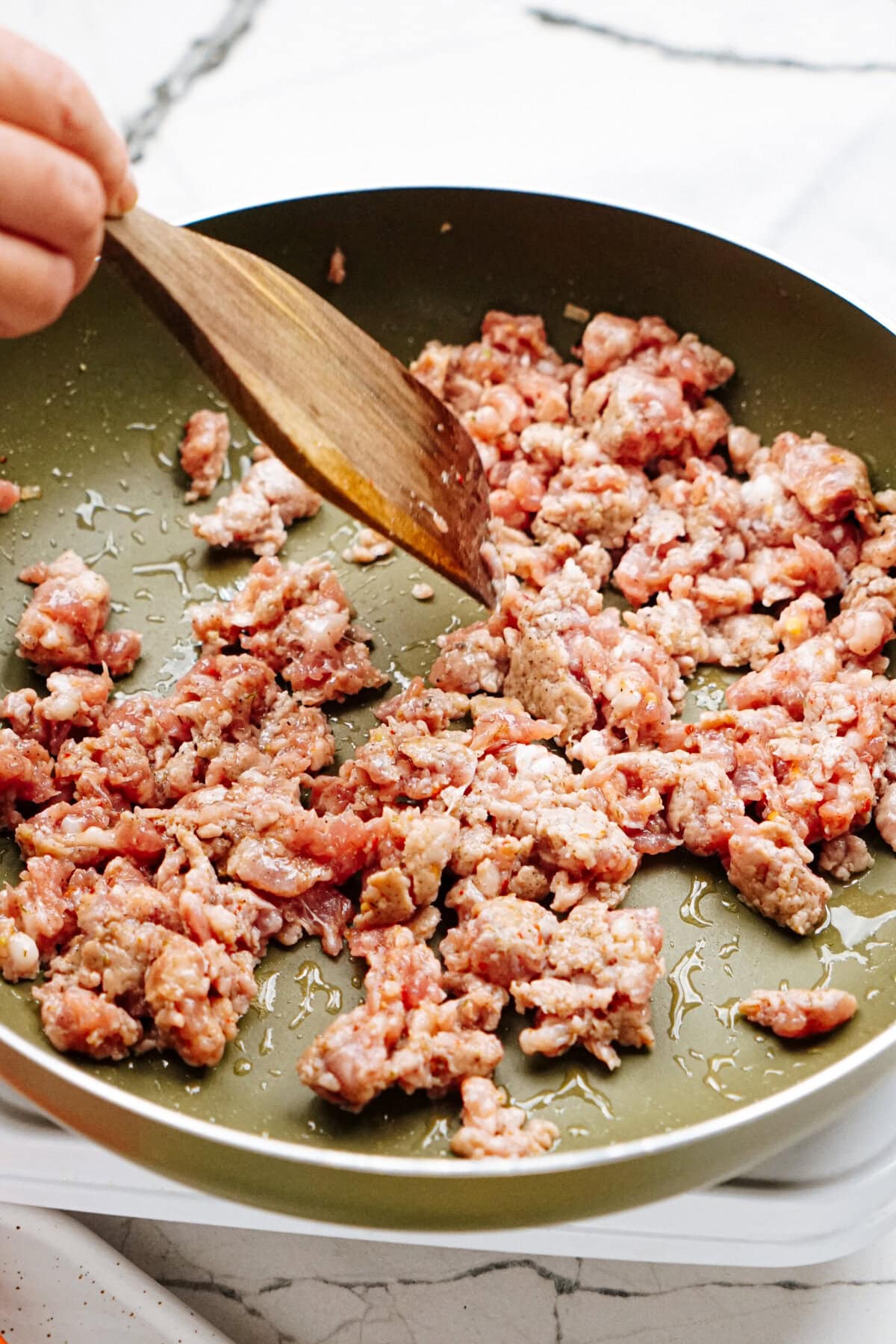 A person stirs ground meat with a wooden spatula in a green frying pan.