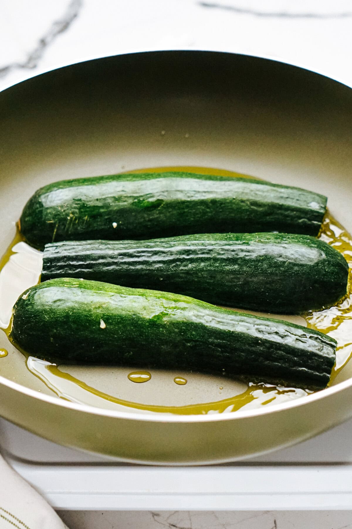 Three whole zucchinis cooking in a pan with oil.