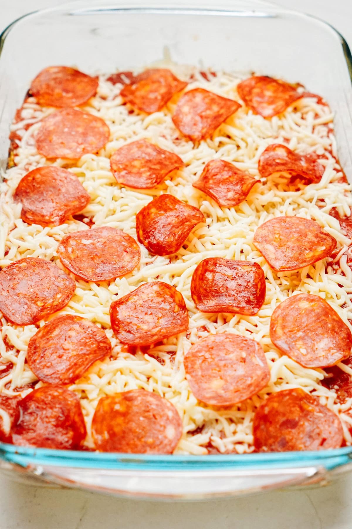 A clear glass baking dish filled with Zucchini Pizza Casserole, topped with layers of shredded cheese and pepperoni slices.