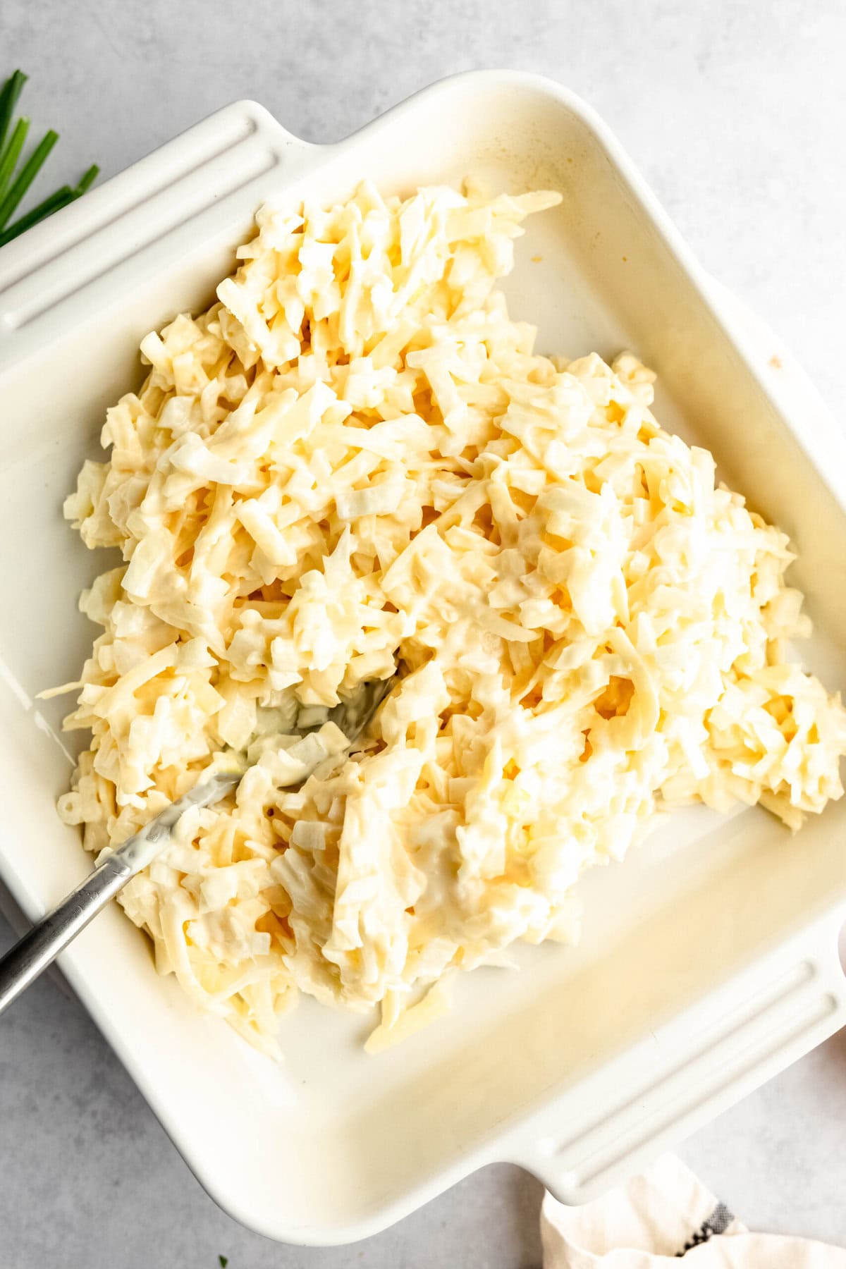 A dish of creamy onion dip with shredded cabbage in a white rectangular serving dish, with a spoon partially visible.