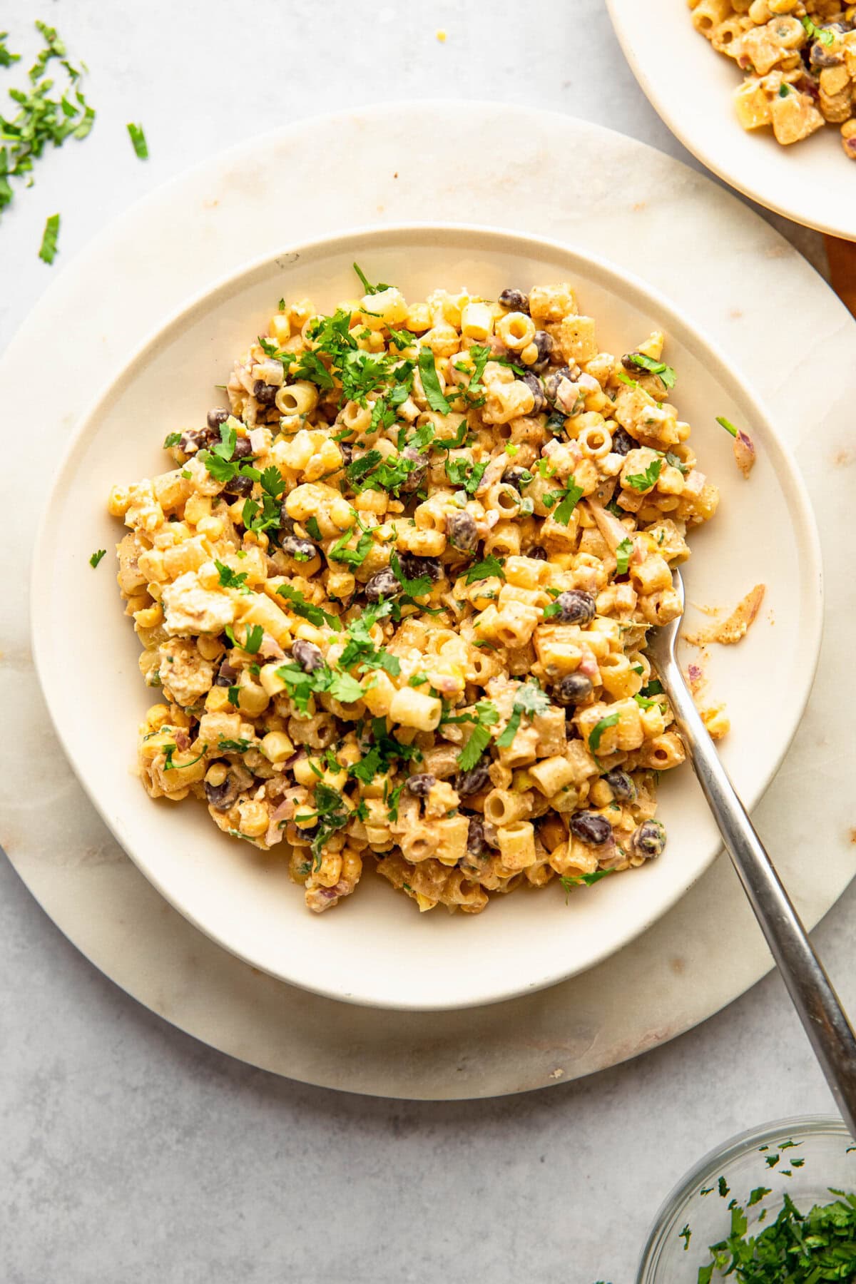 A plate of pasta salad with corn, black beans, and cilantro, served on a white dish with a fork.