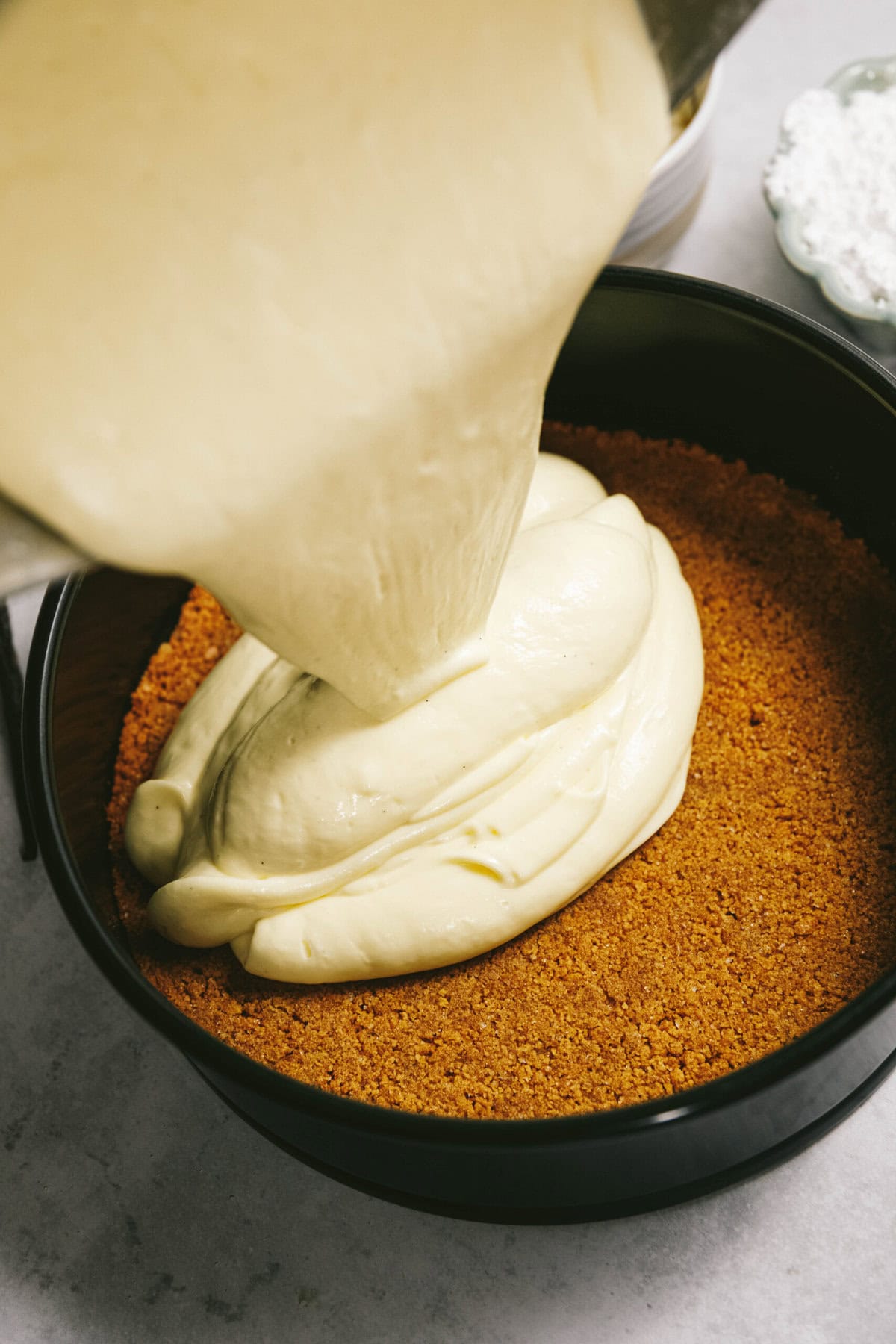 Pouring creamy batter into a pan with a graham cracker crust base.