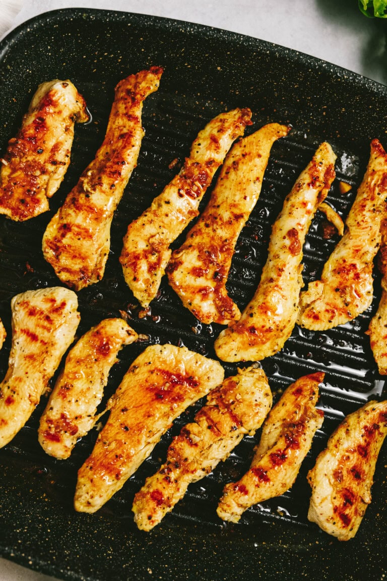 Grilled, seasoned chicken strips cooking on a black grill pan.