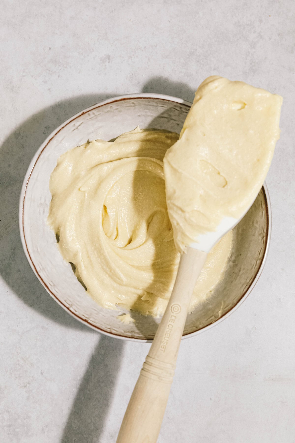 A bowl with thick, creamy batter and a spatula resting on its edge, likely for baking purposes.