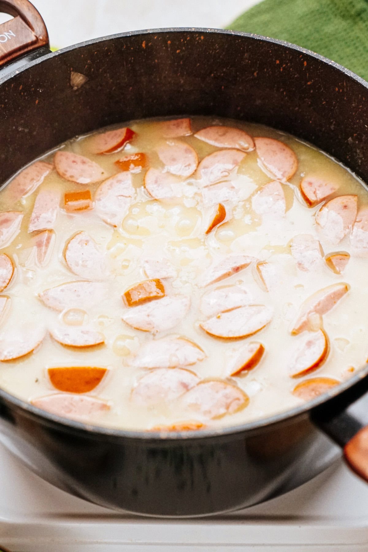 A black pot filled with a creamy soup featuring sliced sausages and diced vegetables.