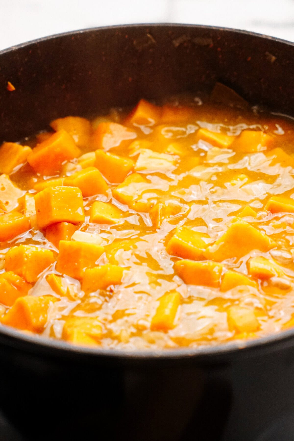 A close-up of a pot filled with thick, chunky orange soup, containing diced pieces of squash or a similar vegetable.