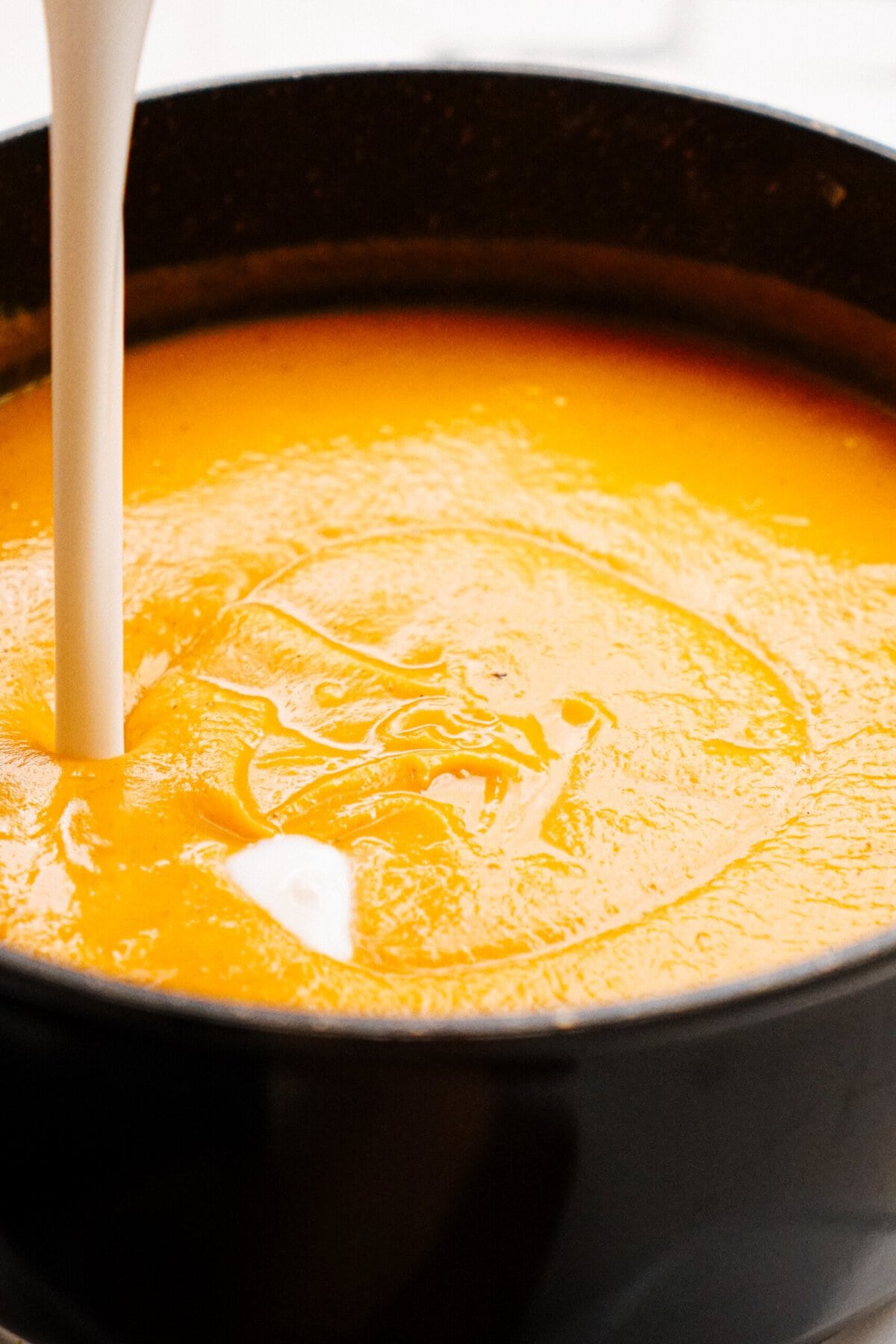 A close-up view of orange soup being poured into a black bowl.