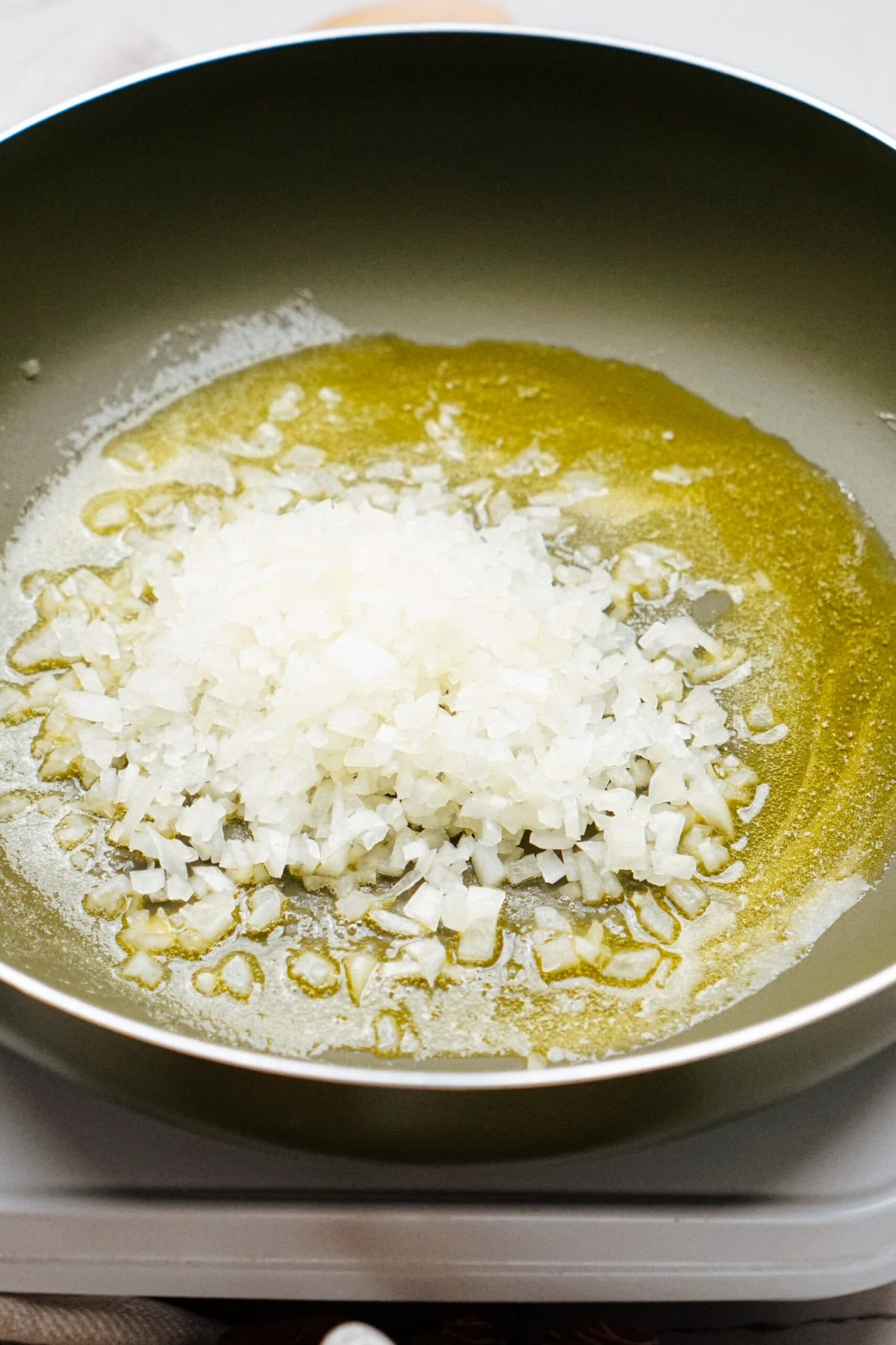 Chopped onions are being sautéed in a frying pan with oil.