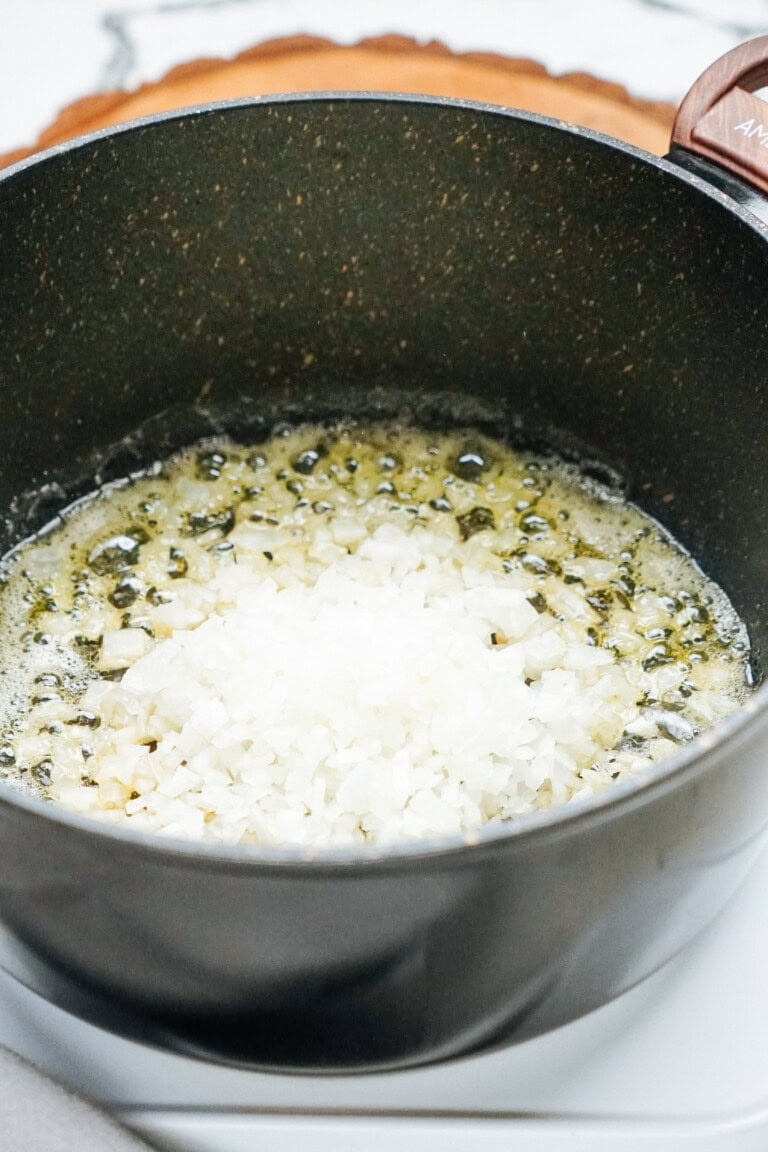 Chopped onions cooking in a black pot with butter.