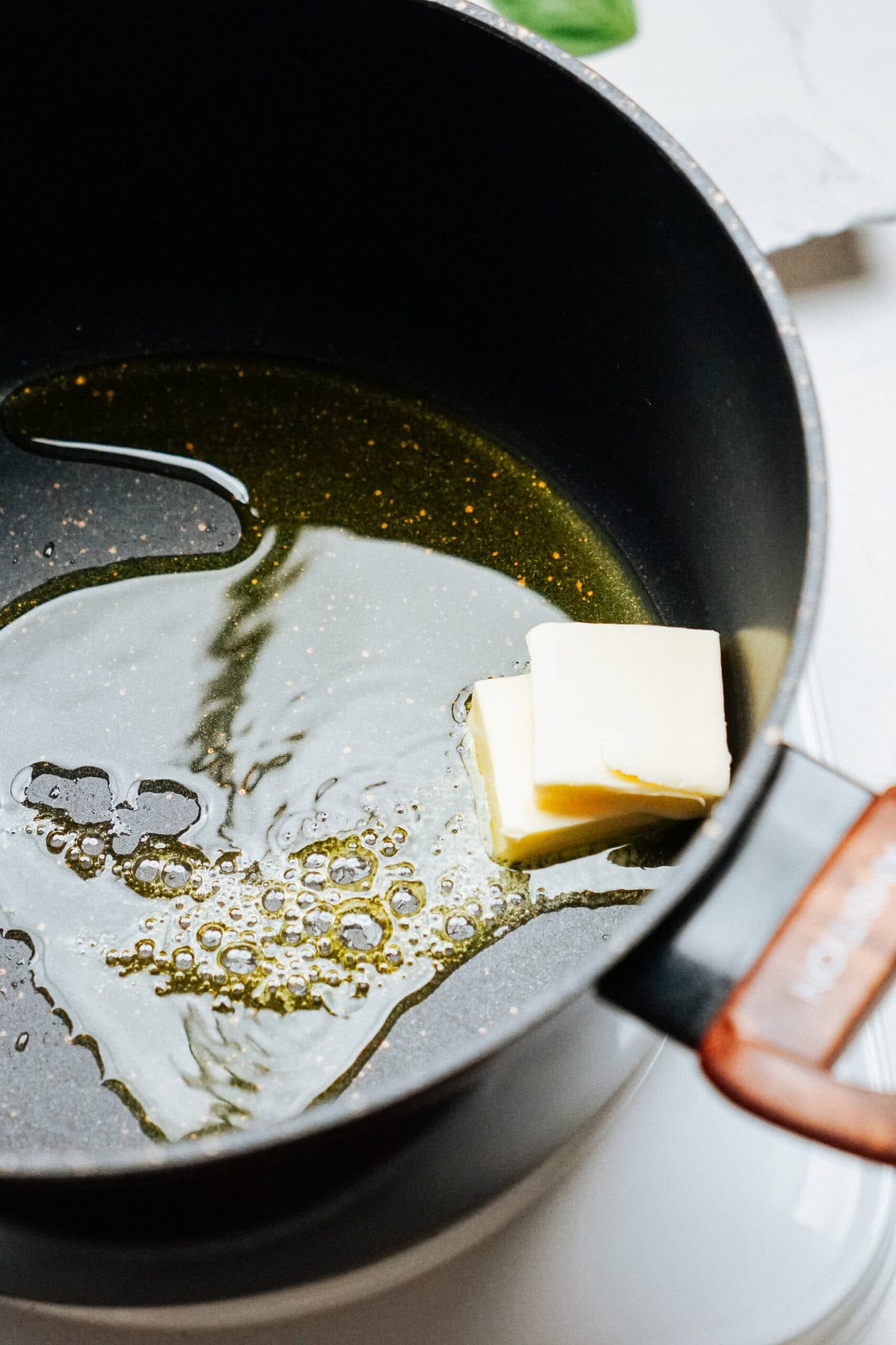 A non-stick pan on a stovetop with melting butter and a small amount of oil.