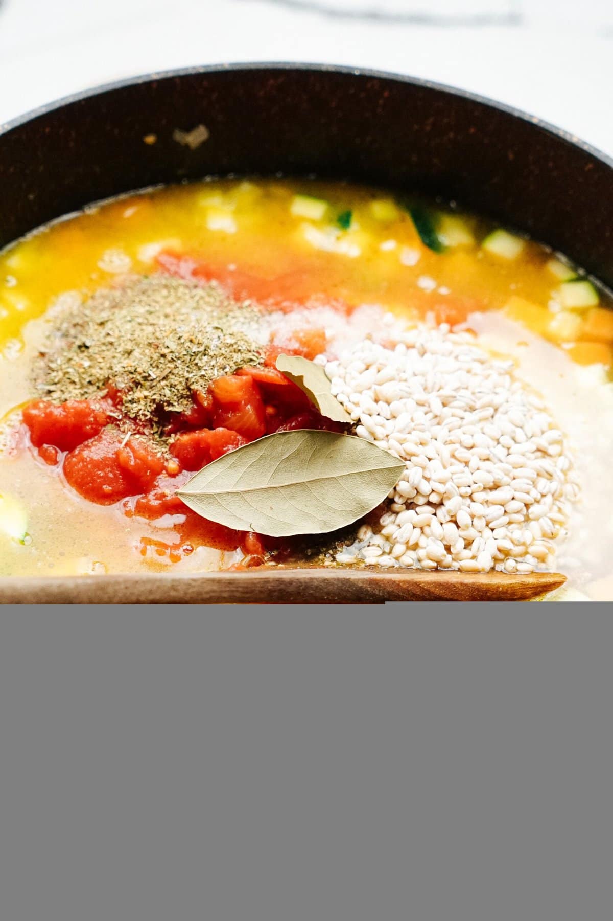 A pot of soup ingredients including tomatoes, grains, bay leaves, and herbs is being prepared.