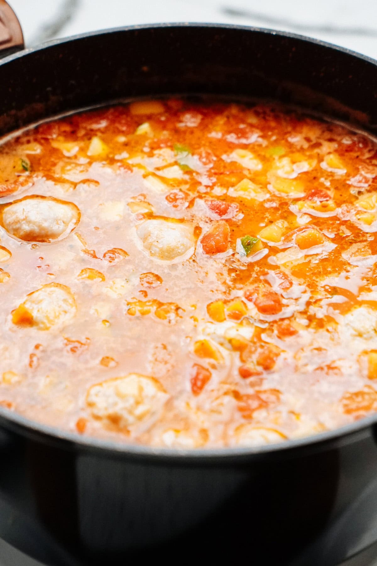 A pot of tomato-based stew with vegetables and meatballs, simmering with visible peppers and herbs.