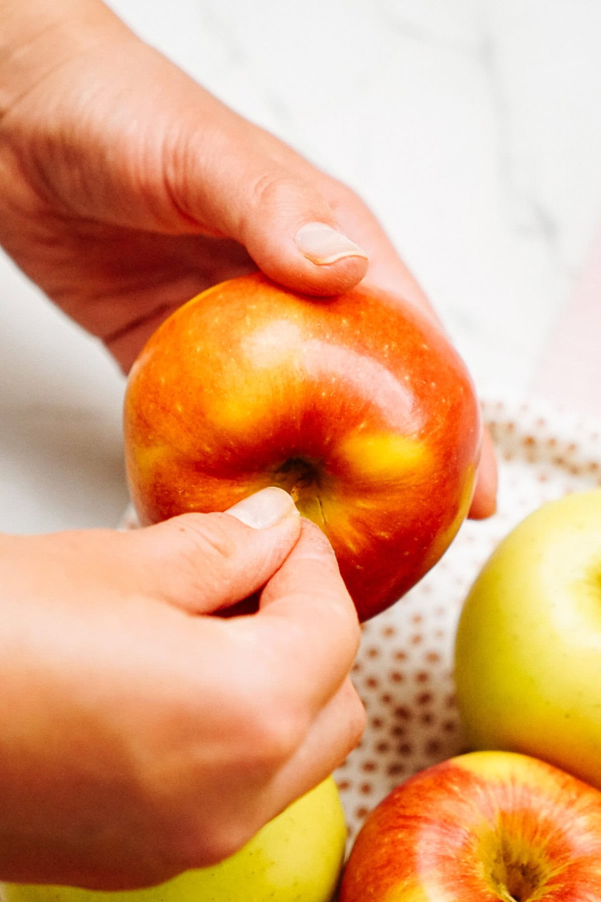 A close-up of hands inspecting a red apple above a bowl containing other gourmet caramel apples.