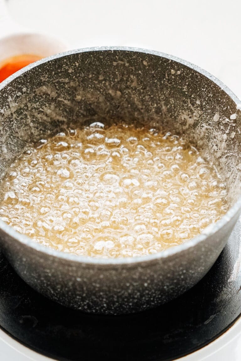 A pot on a stove contains bubbling sugar mixture caramelizing.