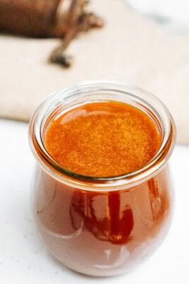 A small glass jar filled with caramel sauce, placed on a light-colored surface.