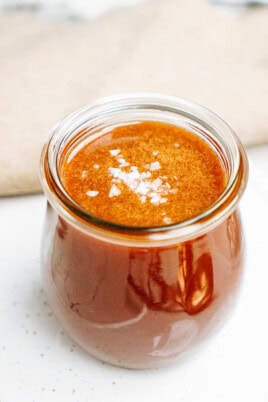 A small glass jar filled with reddish-brown sauce topped with a sprinkling of salt flakes.