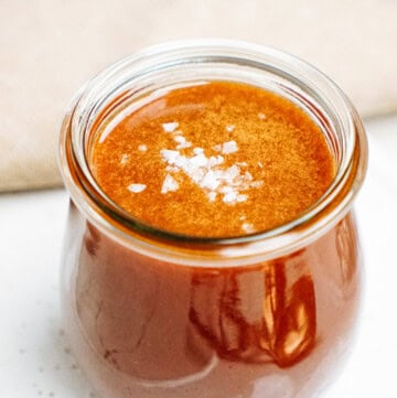 A small glass jar filled with reddish-brown sauce topped with a sprinkling of salt flakes.