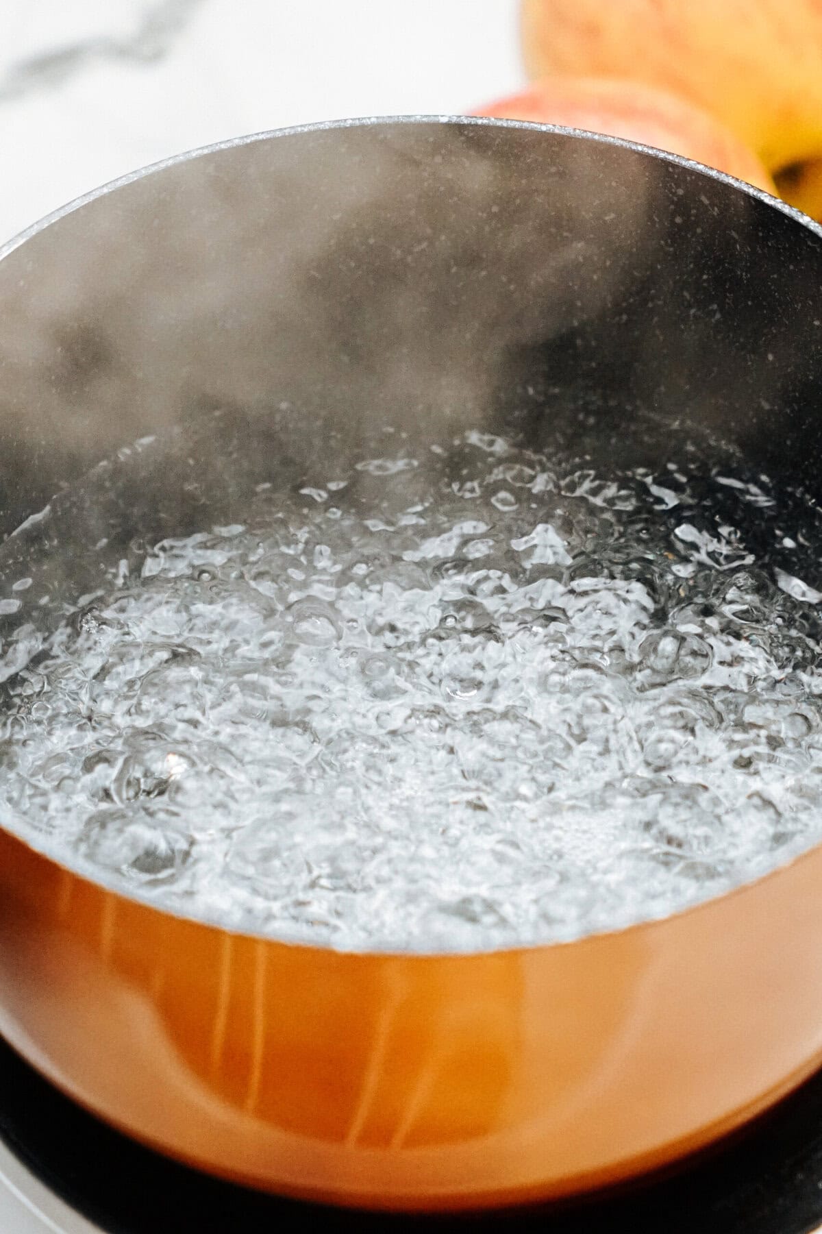 A pot filled with vigorously boiling water sits on a stove, steam swirling above it like the beginning stages of crafting gourmet caramel apples.