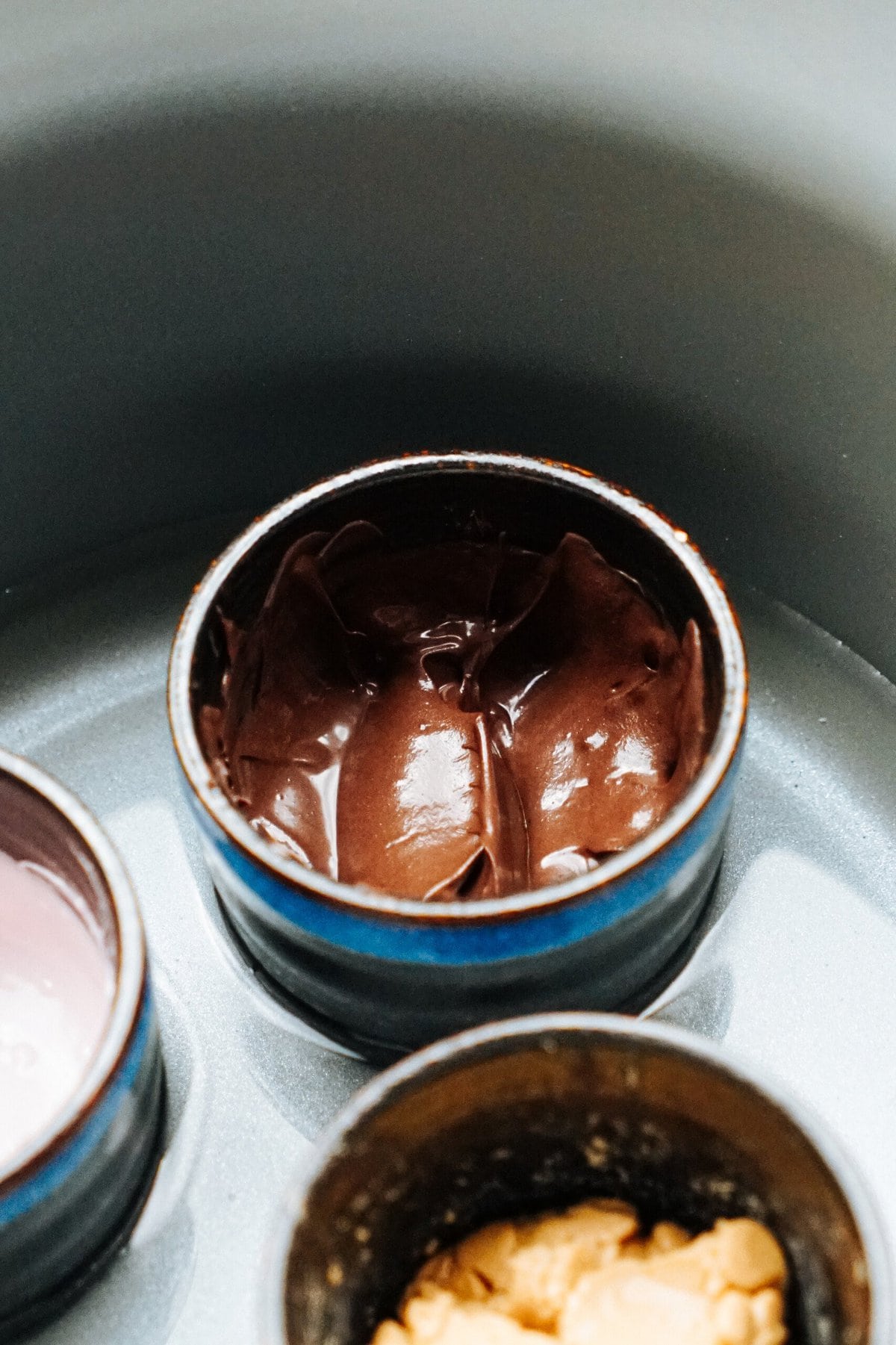 Close-up of a small blue-rimmed bowl filled with chocolate mousse placed next to other bowls containing gourmet caramel apples and various sauces.