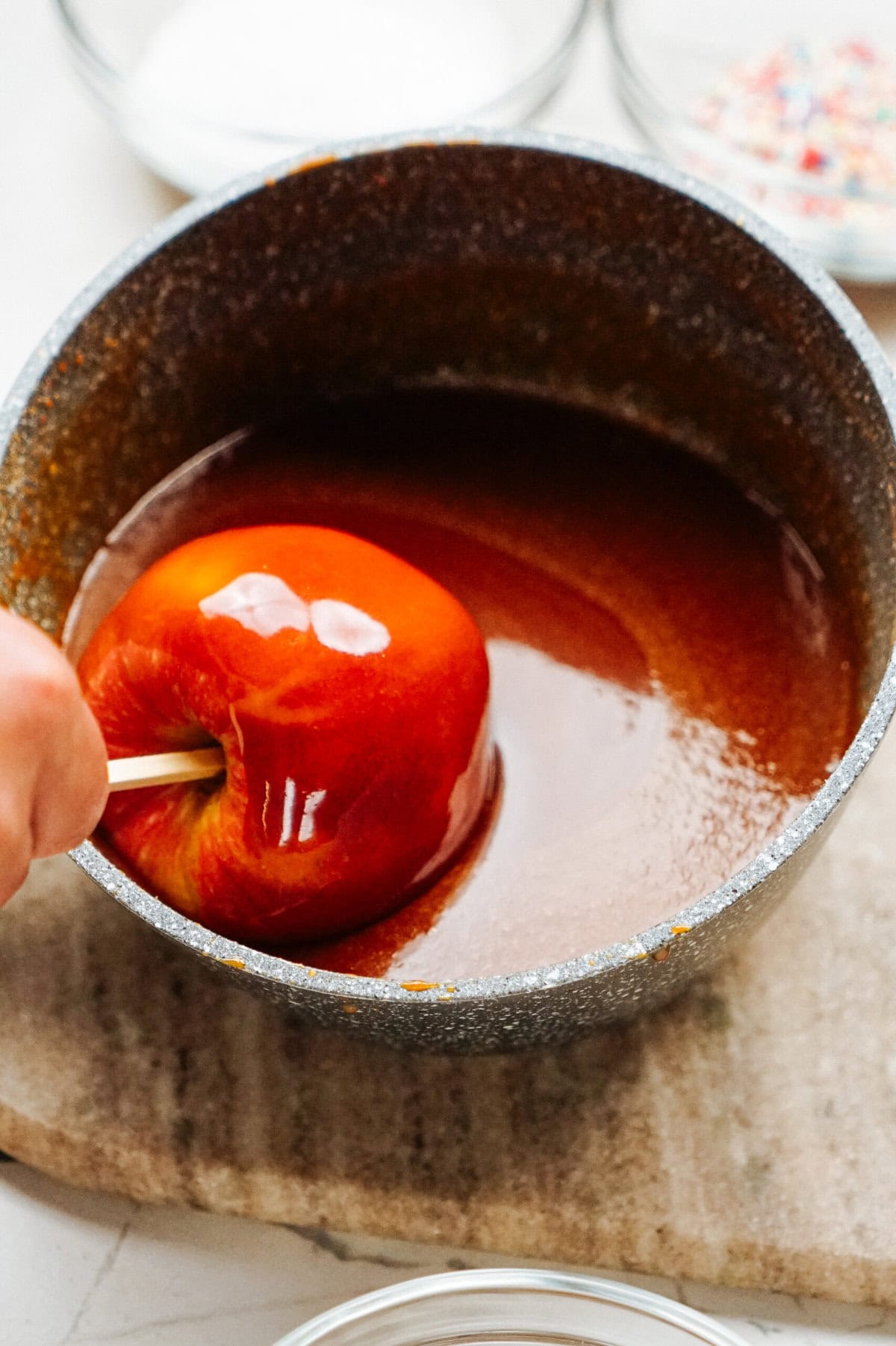 A hand dips an apple into a pot of rich, gourmet caramel.