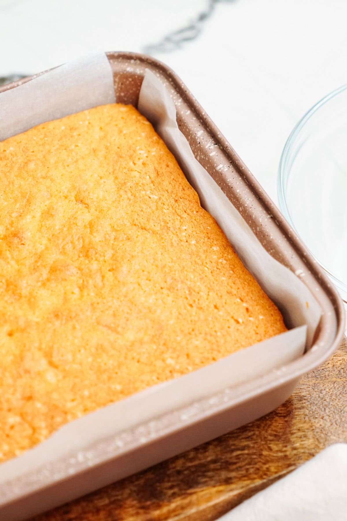 A baked sheet cake, reminiscent of delightful Christmas cake pops, rests in a parchment-lined square baking pan on a wooden surface.